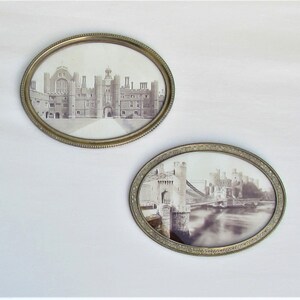 May include: Two oval-shaped antique picture frames with ornate gold-colored metal frames. The frames contain black and white photographs of historic buildings.