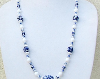 May include: A white and blue beaded necklace displayed on a white mannequin. The necklace features a variety of round and oval beads in white and blue, with intricate floral patterns. The necklace is a delicate piece of jewelry.
