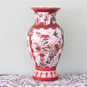 Puede incluir: Un jarrón de cerámica rojo y blanco con un diseño floral. El jarrón tiene una boca ancha y una base estrecha. Está decorado con flores y hojas rojas y negras, y un pequeño pájaro.