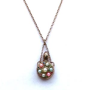 May include: A vintage-style necklace with a delicate chain and a pendant shaped like a small purse. The pendant is adorned with colorful, round beads in shades of pink, green, and white, set in a gold-toned metal frame.