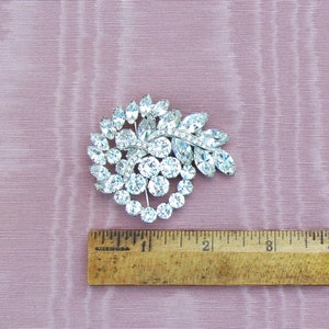 May include: A silver tone brooch with a swirl design featuring clear rhinestones. The brooch is approximately 2 inches in diameter.
