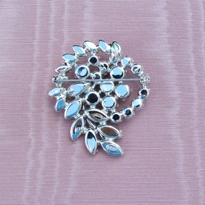 May include: A silver-toned brooch with a swirl design featuring clear and dark gray rhinestones. The brooch is marked "WIESS" on the back.