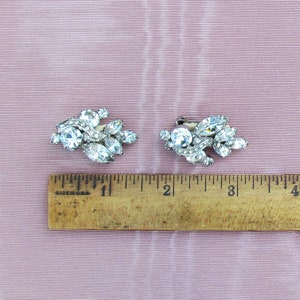 May include: A pair of silver tone rhinestone earrings with a cluster of clear rhinestones in a leaf-like design. The earrings are approximately 1 inch in length.