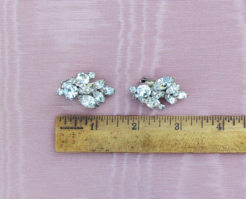 May include: A pair of silver tone rhinestone earrings with a cluster of clear rhinestones in a leaf-like design. The earrings are approximately 1 inch in length.