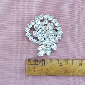 May include: A silver-toned brooch with a cluster of clear rhinestones in a leaf-like design. The brooch is approximately 2 inches in diameter.