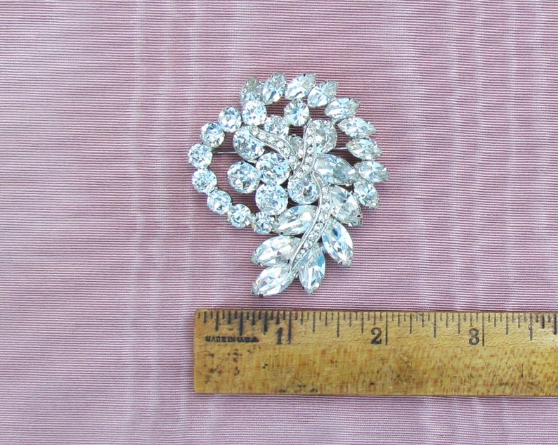 May include: A silver-toned brooch with a cluster of clear rhinestones in a leaf-like design. The brooch is approximately 2 inches in diameter.