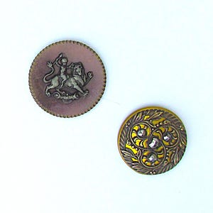 May include: Two antique buttons. One is round with a pinkish-purple background and a silver-colored relief of a person riding a lion. The other is gold-colored with a floral design and three clear rhinestones.