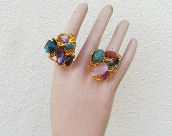 May include: Two gold rings with a cluster of colorful gemstones. The rings feature a variety of stones, including amethyst, rose quartz, turquoise, and brown stones.