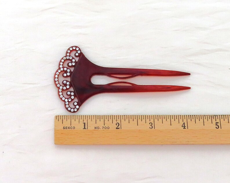 Puede incluir: Una horquilla para el cabello de color burdeos con un dise&ntilde;o de remolino decorativo adornado con pedrer&iacute;a transparente. El accesorio para el cabello mide aproximadamente 12.7 cm de largo y est&aacute; colocado junto a una regla de madera.
