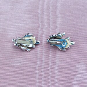 May include: A pair of silver tone clip-on earrings with clear rhinestones. The earrings have a floral design and the back of the earrings are marked "Weiss".