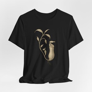 May include: Black t-shirt with a botanical illustration of a pitcher plant. The detailed drawing in shades of tan and brown depicts the plant's leaves, stem, and distinctive pitcher-shaped structure. A unique design for plant lovers.