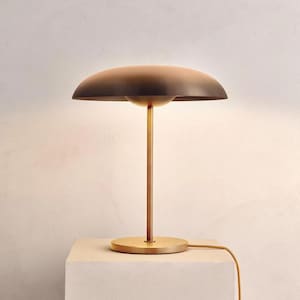 K&ouml;nnte beinhalten: Eine moderne Tischlampe aus Messing mit einem pilzf&ouml;rmigen Schirm. Die Lampe hat einen kreisf&ouml;rmigen Sockel, einen schlanken Stiel und einen gew&ouml;lbten Schirm. Der Schirm hat eine dunkelbraune Farbe, und die Lampe ist an eine Steckdose angeschlossen.