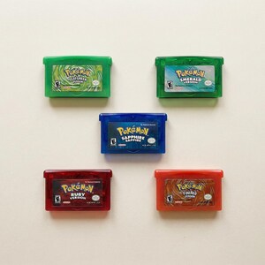 May include: Five colorful Pokemon Game Boy Advance cartridges. The cartridges are green, blue, and red, with the game titles visible. The games include FireRed, LeafGreen, Ruby, Sapphire, and Emerald versions.
