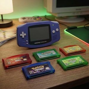 May include: A purple Game Boy Advance handheld console with a black screen and several colorful game cartridges. The cartridges are labeled with the Pokemon series titles, including Ruby, Sapphire, and Emerald versions. The items are on a wooden desk.