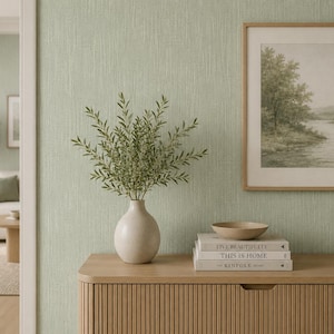May include: A light green room featuring a wooden cabinet, a framed landscape print, and a vase of greenery. The cabinet holds books and a small wooden bowl. The room has a neutral, calming aesthetic.