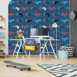 Könnte beinhalten: Ein Raum mit einer blauen Wand mit einem Muster aus Videospiel-Controllern und Konsolen. Vor der Wand befindet sich ein Schreibtisch mit einem Computer, einem Rucksack und einer Spielzeugrakete. Ein Skateboard und ein Teppich liegen auf dem Boden.