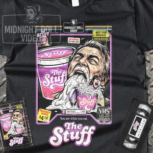 Puede incluir: Camiseta negra con un gráfico de la película "The Stuff". El diseño muestra a un hombre comiendo una sustancia blanca, una taza morada y el texto "The Stuff". También incluye una cinta VHS.