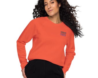 May include: An orange sweatshirt with the word "MAHJONG" printed three times in a stacked design on the upper left chest. The sweatshirt has long sleeves and a crew neck. The person in the image is wearing black pants.
