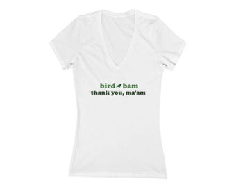 May include: White V-neck t-shirt with the text "bird bam thank you, ma'am" in green. The shirt has short sleeves and a relaxed fit. The text includes a small bird graphic.