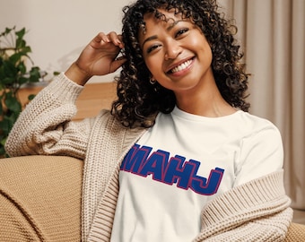 May include: A white short-sleeved t-shirt featuring the text MAHJ printed in bold blue letters with a red outline across the chest. The shirt is worn under a beige knit cardigan, showcasing a simple design with clear, legible lettering.