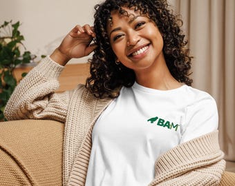 May include: White t-shirt with a green graphic and the letters "BAM". The shirt is made of a soft material. The person is wearing a beige cardigan.