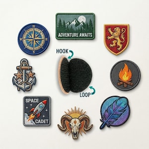 May include: A collection of embroidered patches including a blue compass, a green mountain scene with text ADVENTURE AWAITS, a red lion shield, an anchor, a campfire, a space rocket with text SPACE CADET, a ram skull, and a feather, plus a hook and loop fastener.