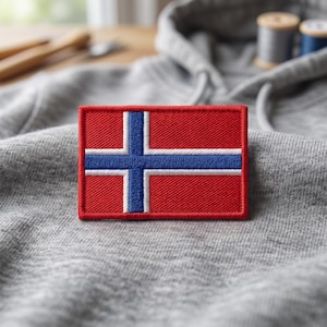 Op de afbeelding: Een rechthoekige geborduurde patch met de vlag van Noorwegen, bestaande uit een rode achtergrond, een blauw kruis en witte randen. De patch heeft een dichte draadstructuur en een dikke, verhoogde rode rand rondom de gehele omtrek.