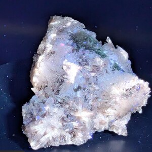 May include: A cluster of crystalline formations, predominantly white with hints of blue, green, and iridescent hues. The crystals have a rough, textured appearance, with sharp, pointed edges. The overall shape is irregular and organic, suggesting a natural mineral specimen.