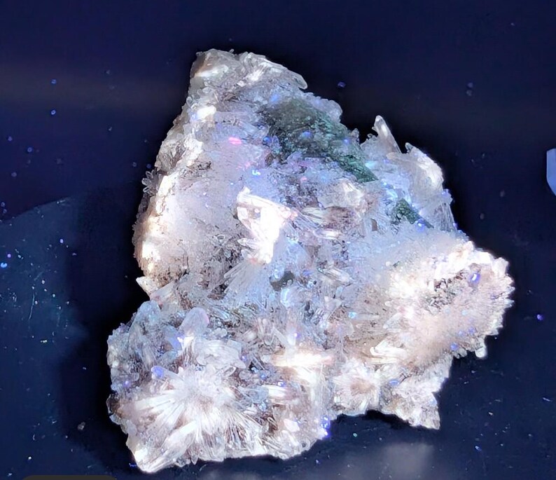 May include: A cluster of crystalline formations, predominantly white with hints of blue, green, and iridescent hues. The crystals have a rough, textured appearance, with sharp, pointed edges. The overall shape is irregular and organic, suggesting a natural mineral specimen.