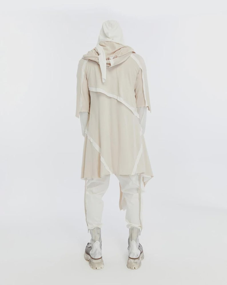 May include: A cream-colored hooded jacket with white trim and matching pants. The jacket has an asymmetrical design and short sleeves. The pants have a zipper detail at the ankles. The outfit is paired with silver and gray boots.