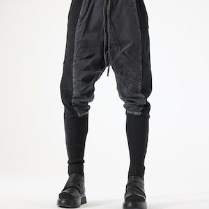 Könnte beinhalten: Schwarze Hose mit tiefem Schritt, einem verwaschenen anthrazitfarbenen Mittelteil mit diagonalen Steppnähten, einem elastischen Kordelzugbund und eng anliegenden, gerippten Beinabschlüssen, kombiniert mit schwarzen Plateau-Schlupfschuhen.