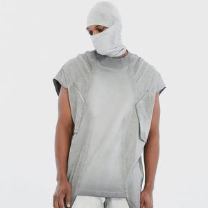 May include: A gray sleeveless top and matching head covering. The top has a unique design with visible seams and a faded appearance. The head covering includes a balaclava and face mask. The outfit is a monochromatic, modern design.