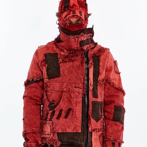 May include: A red distressed jacket with dark brown patches and a matching cap. The jacket has a zip, pockets, and frayed edges. The cap covers the head and face, with eyes visible.