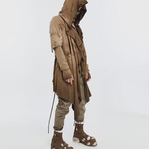 May include: A brown hooded coat with a layered design, long sleeves, and a drawstring. The outfit includes matching pants and unique brown and white patterned shoes. The clothing has a distressed, textured appearance.