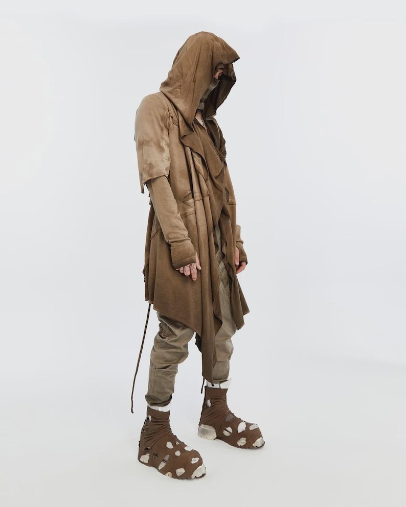 May include: A brown hooded coat with a layered design, long sleeves, and a drawstring. The outfit includes matching pants and unique brown and white patterned shoes. The clothing has a distressed, textured appearance.