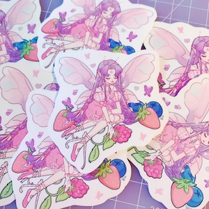 Può includere: Una collezione di adesivi con una fata dai lunghi capelli viola, che indossa un vestito rosa, seduta vicino a fragole, lamponi e mirtilli. La fata ha grandi ali delicate ed è circondata da farfalle. Gli adesivi hanno una palette di colori pastello.