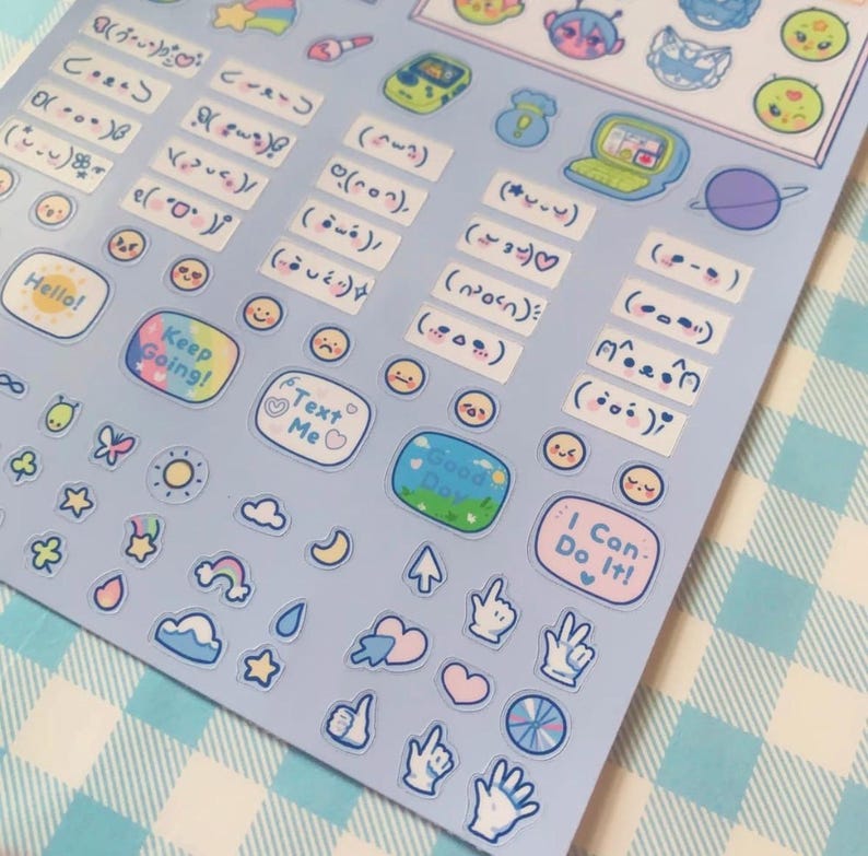 May include: A sheet of pastel-colored stickers with various designs. Includes text bubbles with phrases like "Hello!" and "Keep Going!", along with cute illustrations of stars, clouds, and smiley faces. The stickers are on a light blue background.