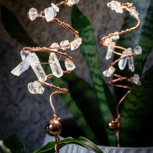 May include: Copper wire plant stakes, each featuring clear quartz crystals and a small copper-colored bell. The spiral design adds a decorative touch to indoor plants. The stakes are approximately 10 inches tall.