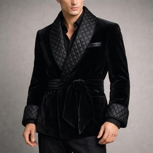 May include: A black velvet robe with a quilted shawl collar, cuffs, and pocket trim. The robe features a matching belt and is worn over a black shirt. The robe's design is classic and elegant.