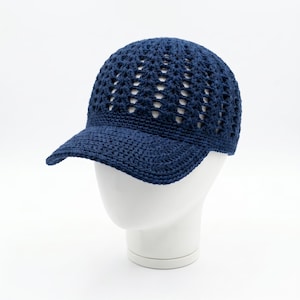 May include: A navy blue crocheted baseball cap with a curved brim. The cap features an open weave design, allowing for ventilation. The hat is displayed on a white mannequin head against a white background.