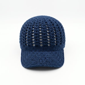 May include: A dark blue baseball cap crafted from crocheted yarn. The crown features an open, airy lattice stitch pattern, while the brim is constructed with a dense, solid crochet stitch. The design is uniform in color and texture throughout.