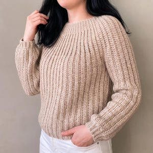 Può includere: Un maglione beige a maniche lunghe caratterizzato da un motivo a maglia a coste verticali su tutto il corpo e le maniche. Il capo presenta uno scollo rotondo e polsini aderenti ai polsi, realizzati con un punto testurizzato che crea un design a linee verticali coerente su tutto il pezzo.
