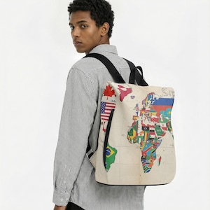 Könnte beinhalten: Beiger Rucksack mit Weltkarten-Design und verschiedenen Nationalflaggen. Er hat einen schwarzen Reißverschluss und Träger. Der Text "34C" ist sichtbar. Der Rucksack wird über den Schultern getragen.