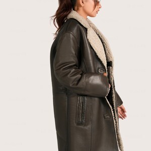 May include: A dark brown leather coat with a cream-colored shearling lining and collar. The coat has a button closure and a classic, oversized design. The long coat is a stylish outerwear piece.