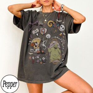 May include: A charcoal gray oversized t-shirt featuring a graphic print of characters from The Nightmare Before Christmas, including Jack Skellington, Sally, Oogie Boogie, and Zero, with the text Nightmare arranged in a circular pattern.
