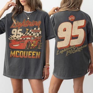 Puede incluir: Camiseta gris oscuro con un dise&ntilde;o de Rayo McQueen de la pel&iacute;cula Cars. El dise&ntilde;o frontal incluye el n&uacute;mero 95, una bandera a cuadros y el nombre McQueen. La parte trasera de la camiseta muestra un gran n&uacute;mero 95 y las palabras "Lightning McQueen".