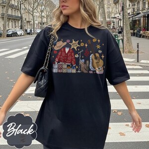 Pode incluir: Uma t-shirt preta de manga curta com uma estampa gr&aacute;fica de um chap&eacute;u de cowboy bege, um cardig&atilde; vermelho com padr&atilde;o paisley, um distintivo de xerife "Sheriff Taylor", uma guitarra ac&uacute;stica castanha, uma bota de cowboy e blocos "TOY STORY".