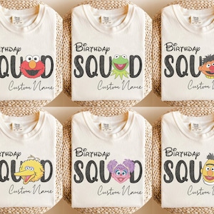 Könnte beinhalten: Sechs cremefarbene T-Shirts mit dem schwarzen Schriftzug Birthday SQUAD, wobei bei jedem Design ein anderer Charakter aus der Sesamstraße den Buchstaben A ersetzt. Darunter steht der Schriftzug Custom Name in schwarzer Schreibschrift.