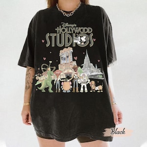 Può includere: T-shirt nero con la scritta "Disney's Hollywood Studios" e una grafica dei personaggi di Toy Story e delle attrazioni del parco. La maglietta ha un aspetto vintage e usurato.