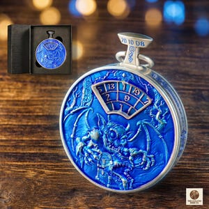 Pode incluir: Um relógio de bolso azul detalhado com uma moldura e detalhes prateados. O mostrador do relógio apresenta uma figura demoníaca e um visor de data. O relógio é apresentado numa caixa preta e tem cerca de 5 cm de diâmetro.